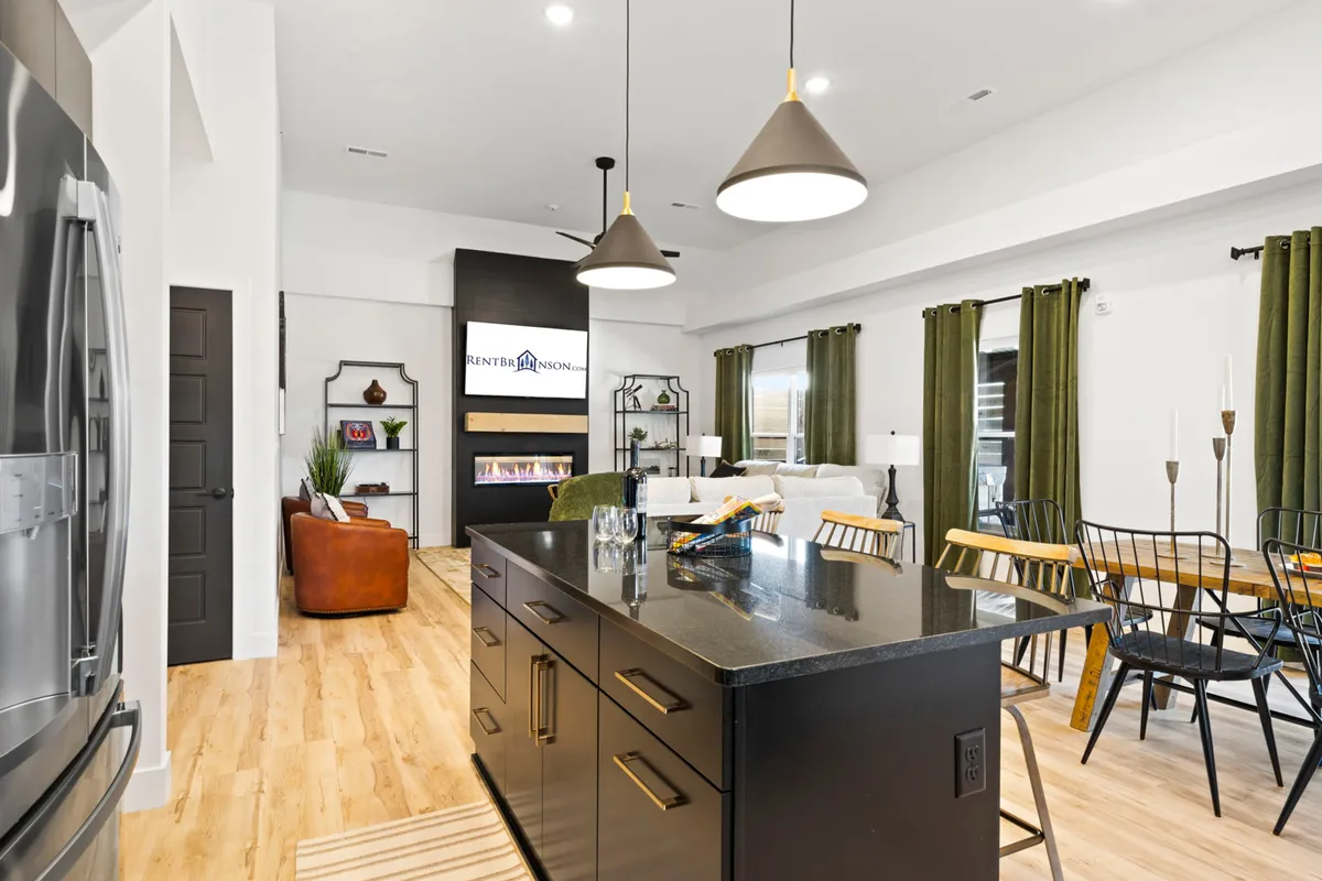 A spacious open-plan area featuring a kitchen island, dining table with high-backed chairs, an inviting living space, and an electric fireplace. The setting is styled for both family relaxation and entertaining, with warm lighting and thoughtful decor touches.