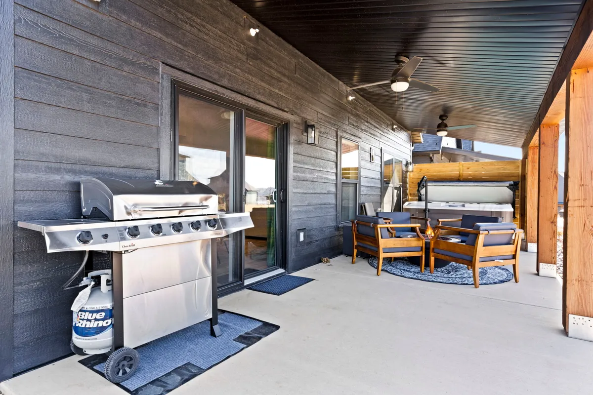 A spacious exterior area with a modern grill, comfortable seating, and a fire pit, surrounded by lush landscaping. The setup invites guests to enjoy barbecues, outdoor dining, and leisurely evenings by the fire.