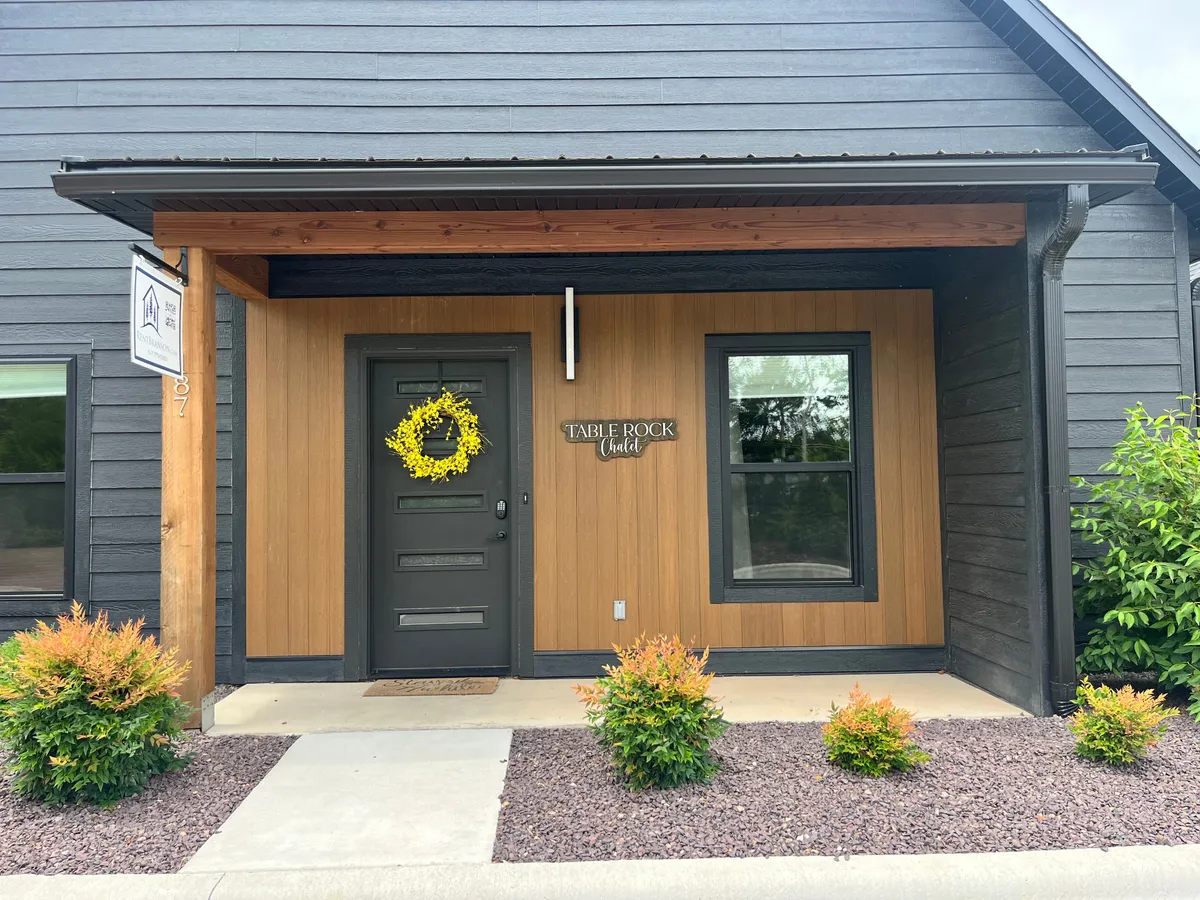 A welcoming front entry with a wreath on the door, a sign reading 'TABLE ROCK chalet,' and landscaping with shrubs. This scene creates a sense of arrival and friendly atmosphere.
