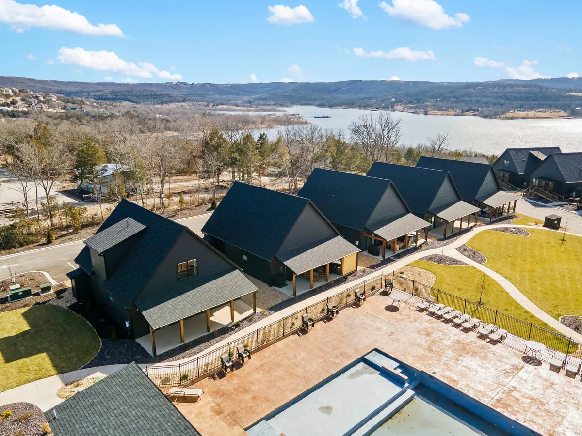 This scene features a row of modern cabins, a swimming pool, green lawn, and an expansive lake view beyond. The layout suggests space for picnics, nature walks, swimming, and tranquil gatherings, all set against the picturesque lake.
