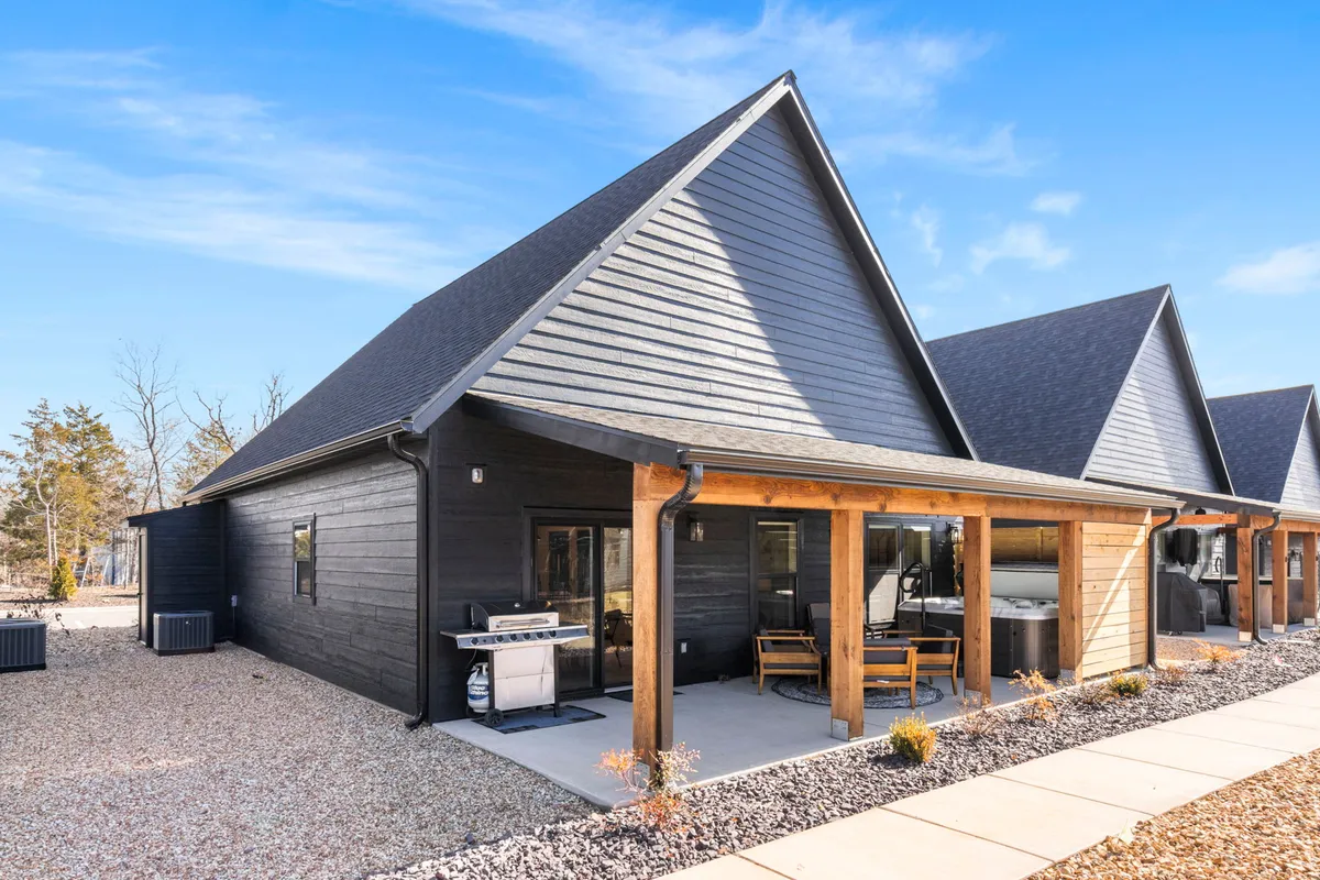 An inviting exterior shot of a modern black chalet with a wooden porch, furnished with outdoor seating and a grill. The setup highlights opportunities for grilling, relaxing outdoors, and gathering with friends or family, all with the natural environment as a backdrop.