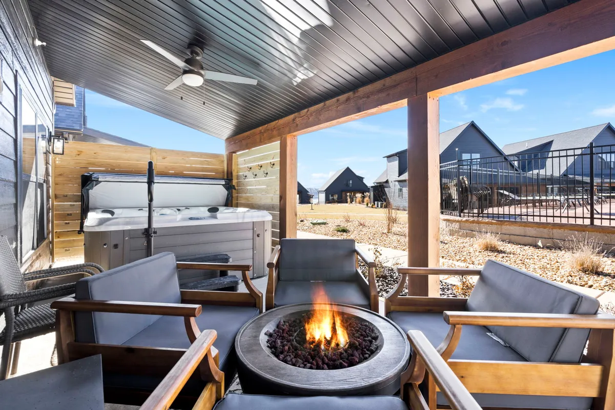 A cozy private deck featuring a fire pit, bubbling hot tub, and outdoor seating. The setting is intimate, with warm lighting ideal for relaxed evenings, story-sharing under the stars, or winding down after a day of adventure.