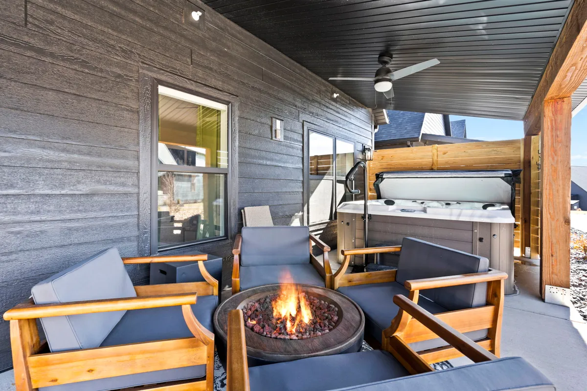 An outdoor space featuring both a fire pit with multiple seating options and a private hot tub, harmoniously arranged for gatherings. The evening lighting creates a warm, cozy atmosphere, perfect for sharing stories or relaxing under the stars.